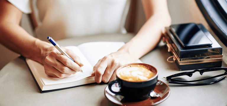 Frau beim täglichen Journaling mit einer Tasse Kaffee